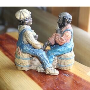 Two African American Men Sitting On Barrels Playing Checkers.